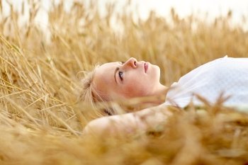 nature, summer holidays, vacation and people concept - young woman or teenage girl lying and dreaming on cereal field