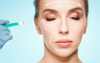 people, cosmetology, plastic surgery and beauty concept - beautiful young woman face and beautician hand in glove with syringe making injection over blue background