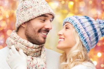 winter, fashion, couple, christmas and people concept - close up of smiling man and woman in hats and scarf hugging over lights background