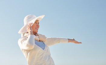 age, leisure and people concept - happy senior woman in sun hat over blue sky