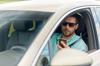 road trip, transport, travel, technology and people concept - man in sunglasses driving car with smartphone