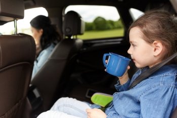 family, transport, road trip and people concept - little girl driving in car with mother and drinking from cup