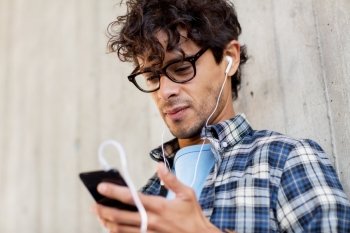 people, music, technology, leisure and lifestyle - happy young hipster man with earphones and smartphone listening to music