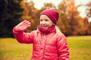 autumn, childhood, gesture, nature and people concept - happy little girl waving hand in park. happy little girl waving hand in autumn park