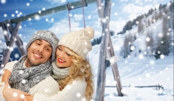 people, christmas, holidays and season concept - happy family couple in winter clothes hugging over wooden swing and snowy mountains background