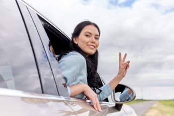 summer vacation, holidays, travel, road trip and people concept - happy young woman driving in car and showing peace sign. happy woman driving in car showing peace sign