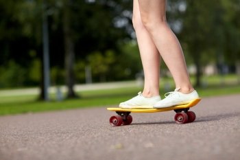 skateboarding, leisure, extreme sport and people concept - close up of teenage girl legs riding short modern cruiser skateboard on road in park