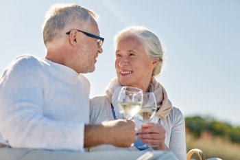family, age, holidays, leisure and people concept - happy senior couple having picnic and clinking wine glasses on summer beach