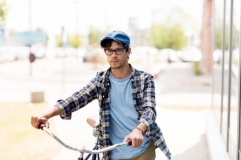 people, style, city life and lifestyle - young hipster man in vintage cap and fixed gear bicycle walking along city on street