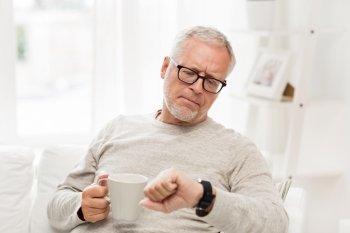 time, morning and people concept - senior man with cup of tea looking at wristwatch at home
