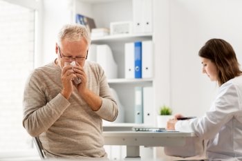 medicine, age, health care, flu and people concept - senior man blowing nose with napkin and doctor with clipboard writing at medical office at hospital