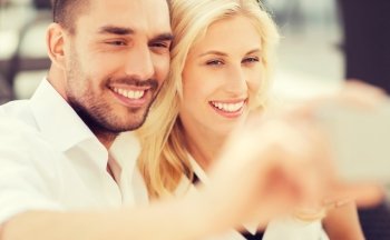 love, date, technology, people and relations concept - smiling happy couple taking selfie with smatphone outdoors