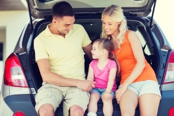 family , transport, leisure, road trip and people concept - happy man, woman and little girl sitting on trunk of hatchback car and talking outdoors