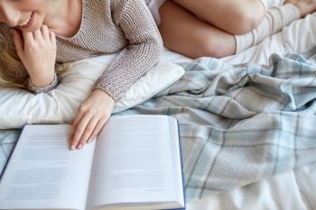 rest, comfort, leisure and people concept - close up of happy young woman reading book in bed at home bedroom