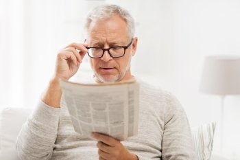leisure, information, people, vision and mass media concept - senior man in glasses reading newspaper at home