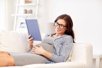 pregnancy and motherhood concept - smiling pregnant woman lying on sofa and reading book. happy pregnant woman reading book at home