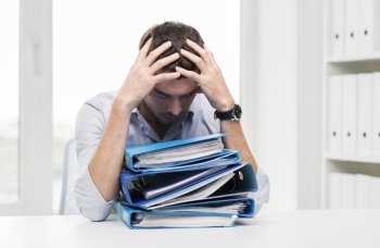 business, people, deadline, stress and paperwork concept - sad businessman with stack of folders at office