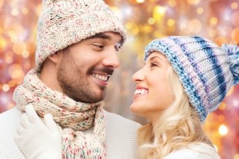 winter, holidays, love, christmas and people concept - close up of smiling man and woman in hats and scarf over lights background