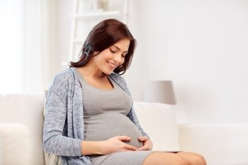 pregnancy, rest, people and expectation concept - happy pregnant woman sitting on sofa at home
