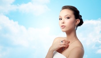 beauty, jewelry, people and luxury concept - beautiful asian woman or bride with earring, finger ring and pendant over blue sky and clouds background