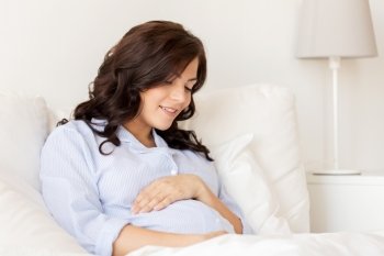 pregnancy, rest, people and expectation concept - happy pregnant woman lying in bed and touching her belly at home