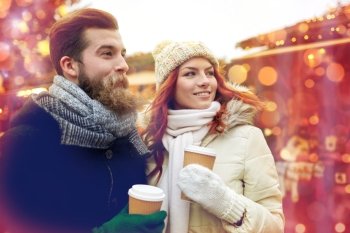 holidays, winter, christmas, hot drinks and people concept - happy couple of tourists in warm clothes drinking coffee from disposable paper cups in old town