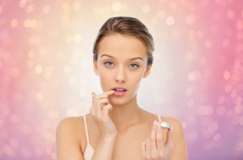 beauty, people and lip care concept - young woman applying lip balm to her lips over rose quartz and serenity lights background