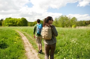 travel, hiking, backpacking, tourism and people concept - happy couple with backpacks walking along country road