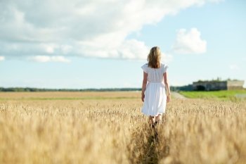 happiness, nature, summer holidays, vacation and people concept - young woman in white dress walking along cereal field