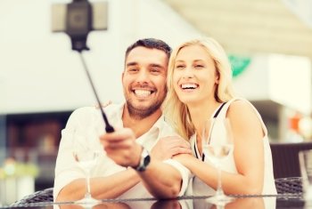 love, date, technology, people and relations concept - happy happy couple taking picture with smartphone on selfie stick at city street cafe or restaurant