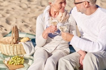 family, age, holidays, leisure and people concept - close up of happy senior couple with picnic basket sitting on blanket on summer beach