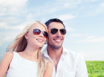 summer holidays, people and dating concept - happy couple in shades over blue sky and grass background
