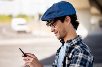 leisure, technology, communication and people concept - smiling hipster man texting message on smartphone on city street