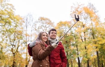 love, technology, relationship, family and people concept - happy smiling couple taking picture by smartphone selfie stick in autumn park
