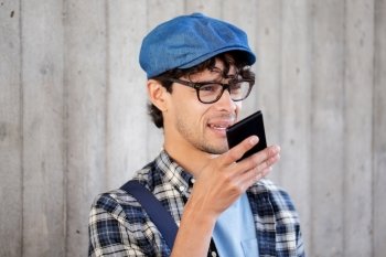 leisure, technology, communication and people concept - smiling hipster man using voice command recorder or calling on smartphone at street wall