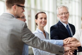 business, people and teamwork concept - smiling business people putting hands on top of each other in office