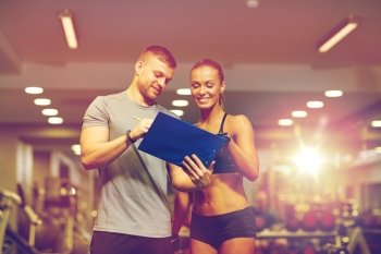 fitness, sport, exercising and diet concept - smiling young woman and personal trainer with clipboard writing exercise plan in gym