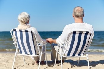 family, old age, travel, tourism and people concept - happy senior couple sitting on deck chairs on summer beach