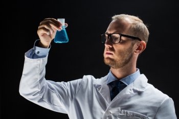 science, chemistry, research and people concept - young scientist holding test flask with chemical over black background