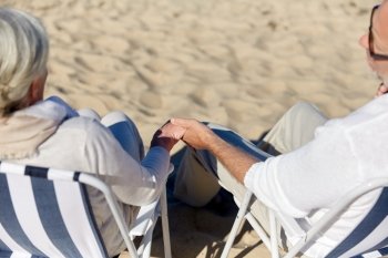 family, old age, travel, tourism and people concept - close up of happy senior couple sitting on deck chairs on summer beach