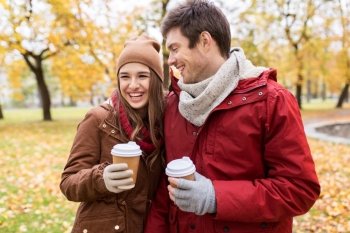 love, relationships, season and people concept - happy young couple with coffee cups walking in autumn park