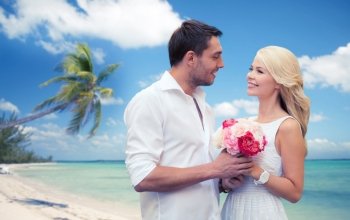 holidays, travel, tourism, people and dating concept - happy couple with bunch of flowers over tropical beach background