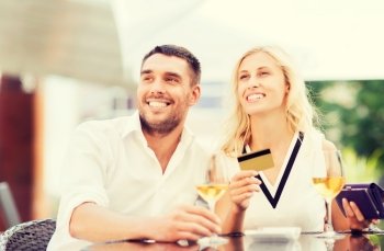date, people, payment and relations concept  - happy couple with credit card, bill and wine glasses at restaurant terrace