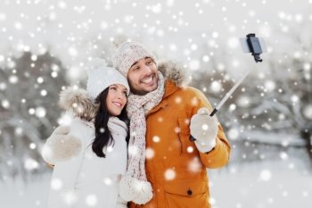 people, season, love, technology and leisure concept - happy couple taking picture with smartphone selfie stick on over winter background