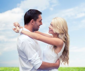 summer holidays, people, love and dating concept - happy couple hugging over blue sky and grass background