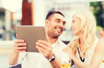 love, dating, people, technology and holidays concept - happy couple with tablet pc computer talking at restaurant lounge or terrace