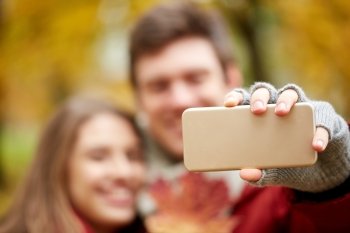love, technology, relationship, family and people concept - happy couple taking selfie by smartphone in autumn park