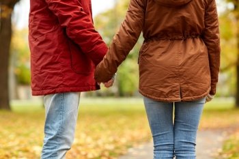 love, relationships, season and people concept - close up of happy young couple holding hands in autumn park
