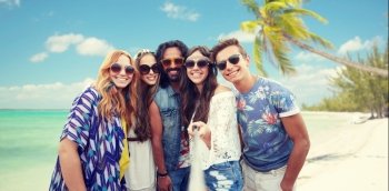 summer vacation, travel, tourism, technology and people concept - smiling young hippie friends taking picture by smartphone selfie stick over beach background