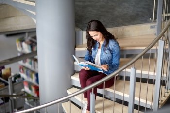 education, high school, university, learning and people concept - smiling student girl reading book sitting on stairs at library